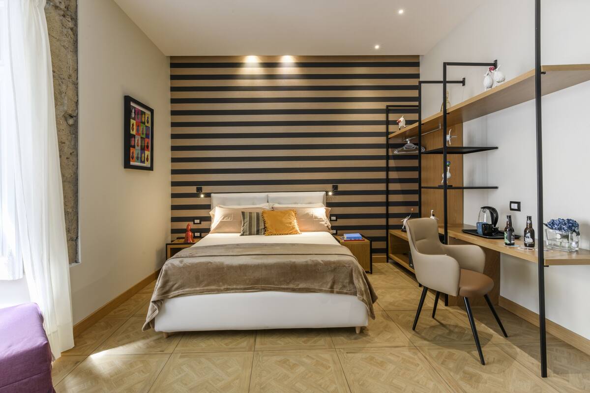 A modern bedroom with a large bed, a desk with a chair, and a shelving unit.