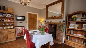 Un comedor con una mesa blanca, sillas rojas, una chimenea y estantes de madera con libros y objetos decorativos.