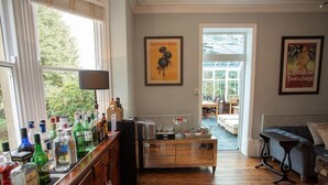 Una habitación con suelo de madera, una zona de bar con varias botellas de licor, un sofá y un comedor con mesa y sillas.