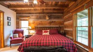 Ein Schlafzimmer in einer Blockhütte mit Bett, Sessel, montiertem Hirschgeweih und einem Fenster mit Blick.