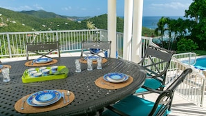 Una mesa de comedor dispuesta con platos, vasos y cubiertos, con vista a una piscina y un paisaje montañoso.