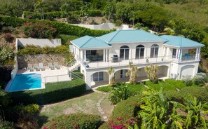 Une grande maison à deux étages, dotée d’une piscine, de nombreux balcons et d’un jardin luxuriant.