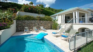 A pool area with lounge chairs, a stone wall, and a building with a balcony. - Southern Breeze: Expansive Ocean Views! Amazing Sunrises! (St. John)