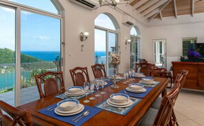 A dining area with a view of the ocean, a large table set for six, and wooden chairs. - Southern Breeze: Expansive Ocean Views! Amazing Sunrises! (St. John)