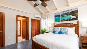 A bedroom with a large bed, wooden headboard, and a view of a coastal landscape. - Southern Breeze: Expansive Ocean Views! Amazing Sunrises! (St. John)