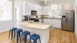 Una cocina moderna con armarios blancos, un refrigerador de acero inoxidable y una isla central con taburetes.