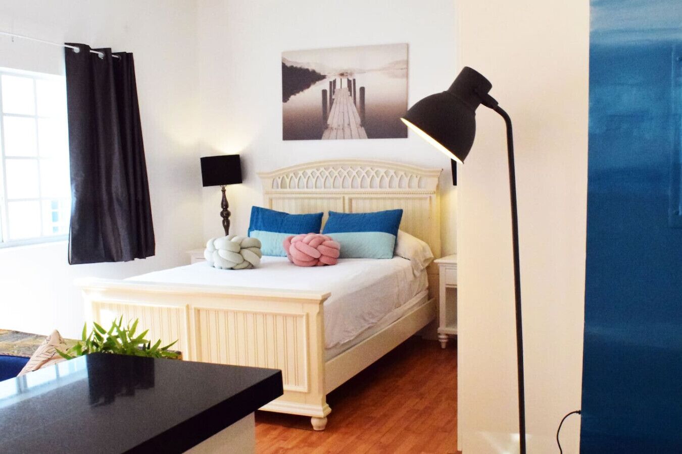 Un dormitorio con una cama, una mesita de noche, una lámpara, una ventana con cortinas y un cuadro colgado en la pared.