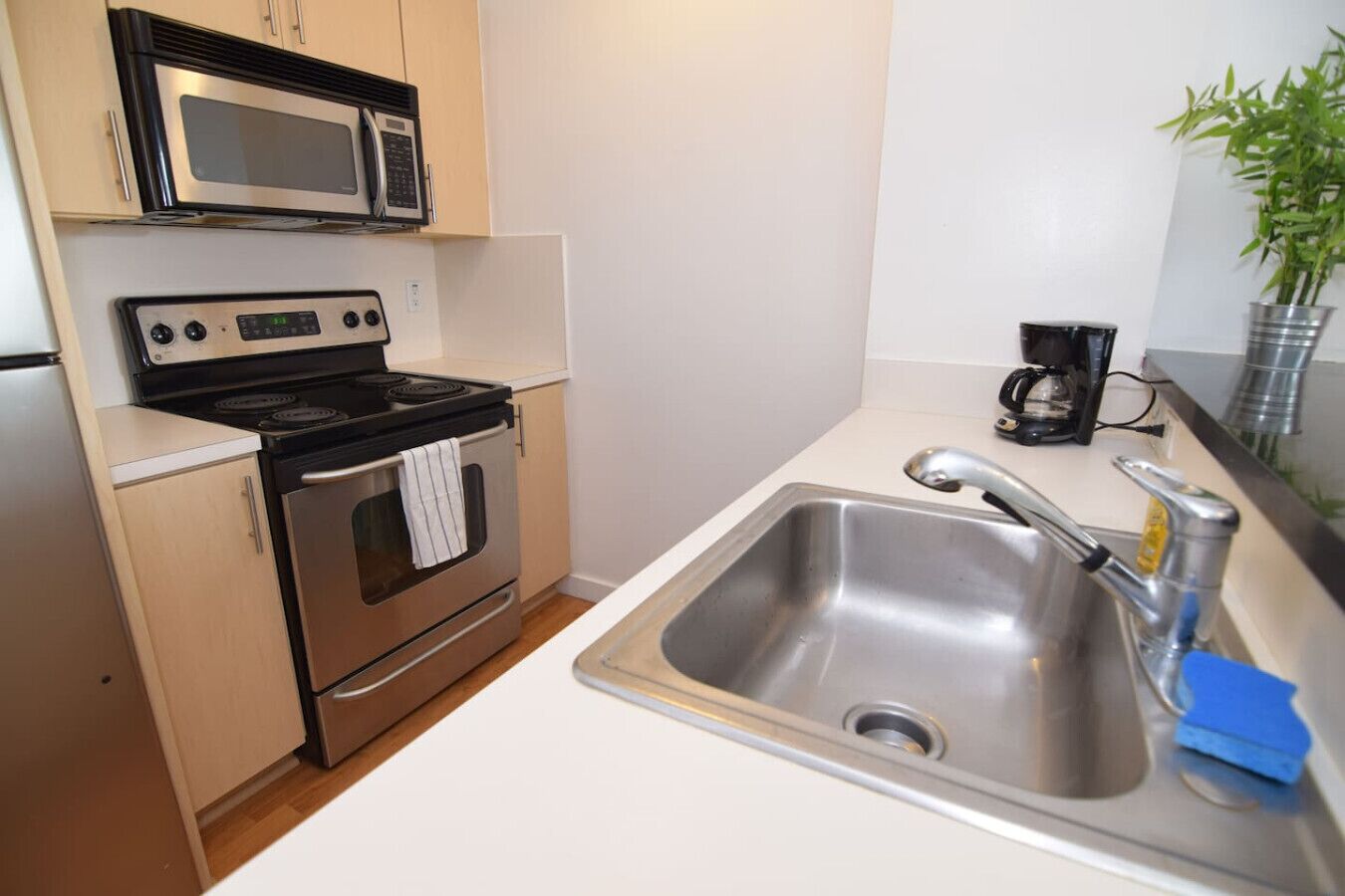 Una cocina compacta con un lavamanos de acero inoxidable, un microondas, un horno y una cafetera.