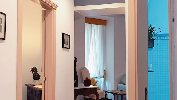 A hallway with a wooden floor, a dining area with a table and chairs, and a bathroom visible through an open door.