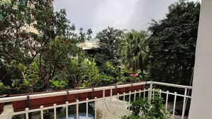 A balcony with a potted plant, a car parked outside, and a view of surrounding greenery and buildings.