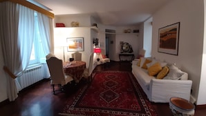 A living room with a dining area, a red patterned rug, a white sofa with yellow cushions, and a table with a red tablecloth.