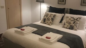 A neatly made bed with white and grey bedding, a lamp, and a door in a room.