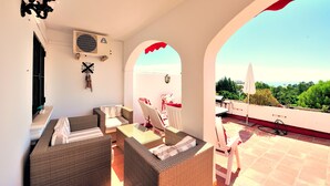 Una terraza en la azotea con muebles de mimbre, un equipo de aire acondicionado y vistas del paisaje.