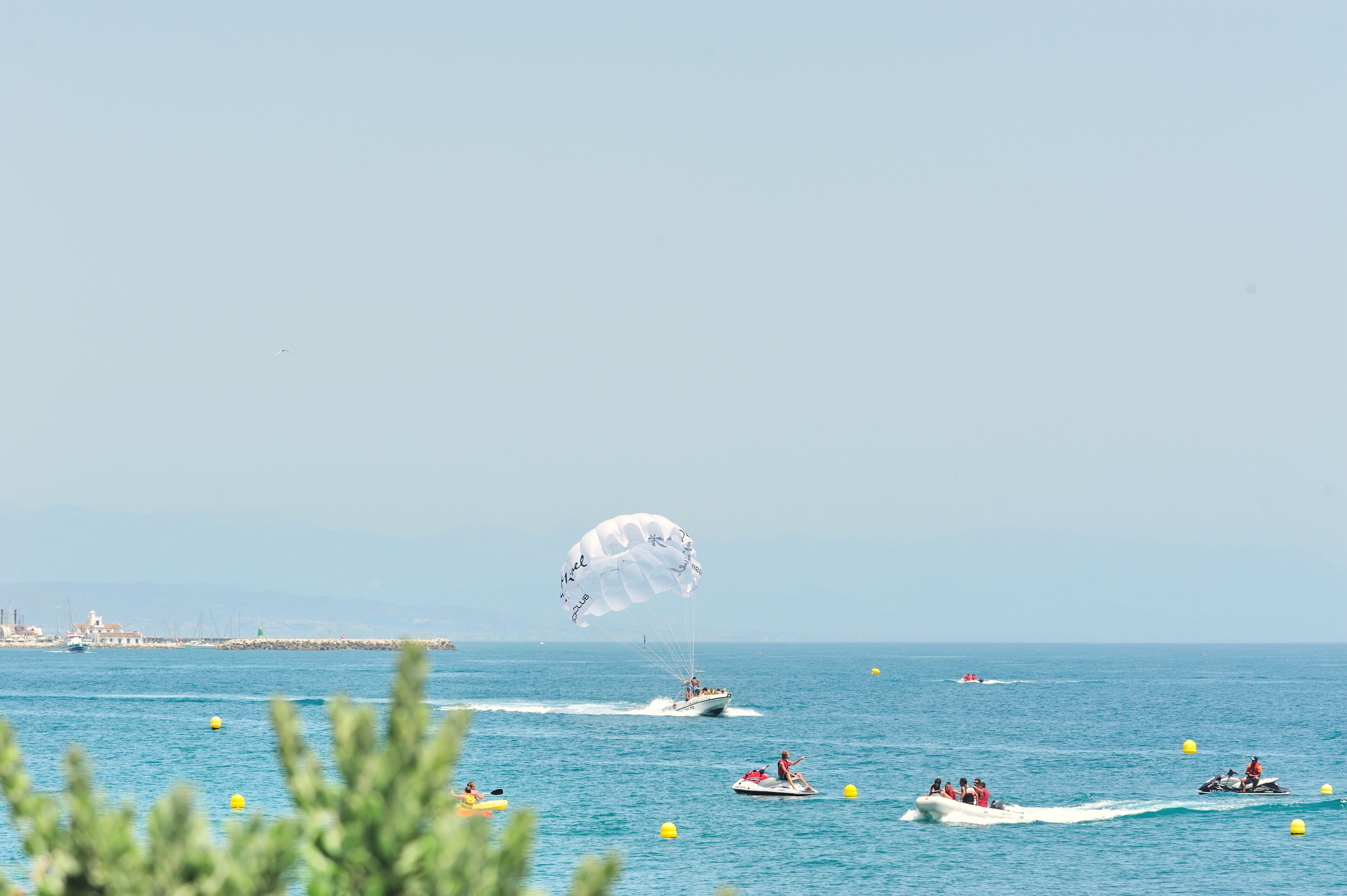 Une scène côtière avec des bateaux et une personne pratiquant le parachute ascensionnel sur l’eau.