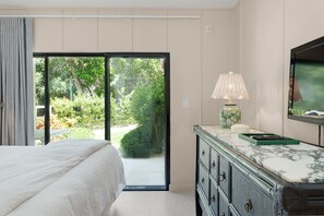 A bedroom with a bed, a dresser, a television, and a sliding glass door leading to a garden.