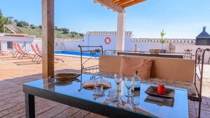 Un área de estar al aire libre con una mesa de vidrio, cojines y vista a una piscina.