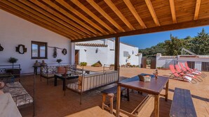 Un espacio de patio al aire libre con una pérgola de madera, una mesa de comedor y sillones reclinables rojos.