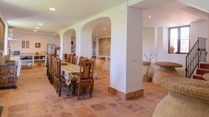 Un comedor amplio con una mesa larga y sillas, una cocina al fondo y una escalera que sube a un nivel superior.
