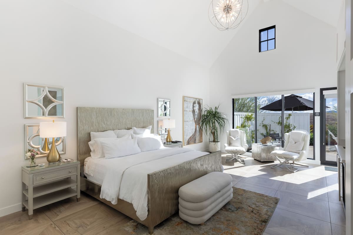 A spacious bedroom with a large bed, a bedside table, a chair, and a view of the outdoors.
