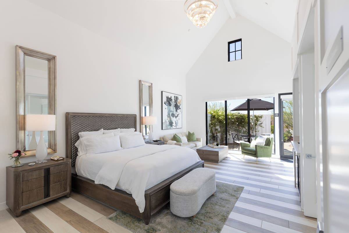 A spacious bedroom with a large bed, a nightstand, a mirror, and a view of the outdoor patio.