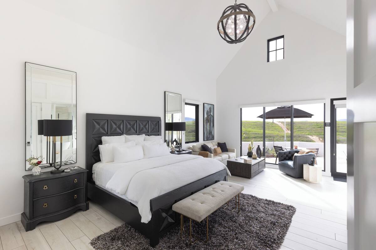 A modern bedroom with a large bed, bedside tables, a bench, and a view of the outdoors.