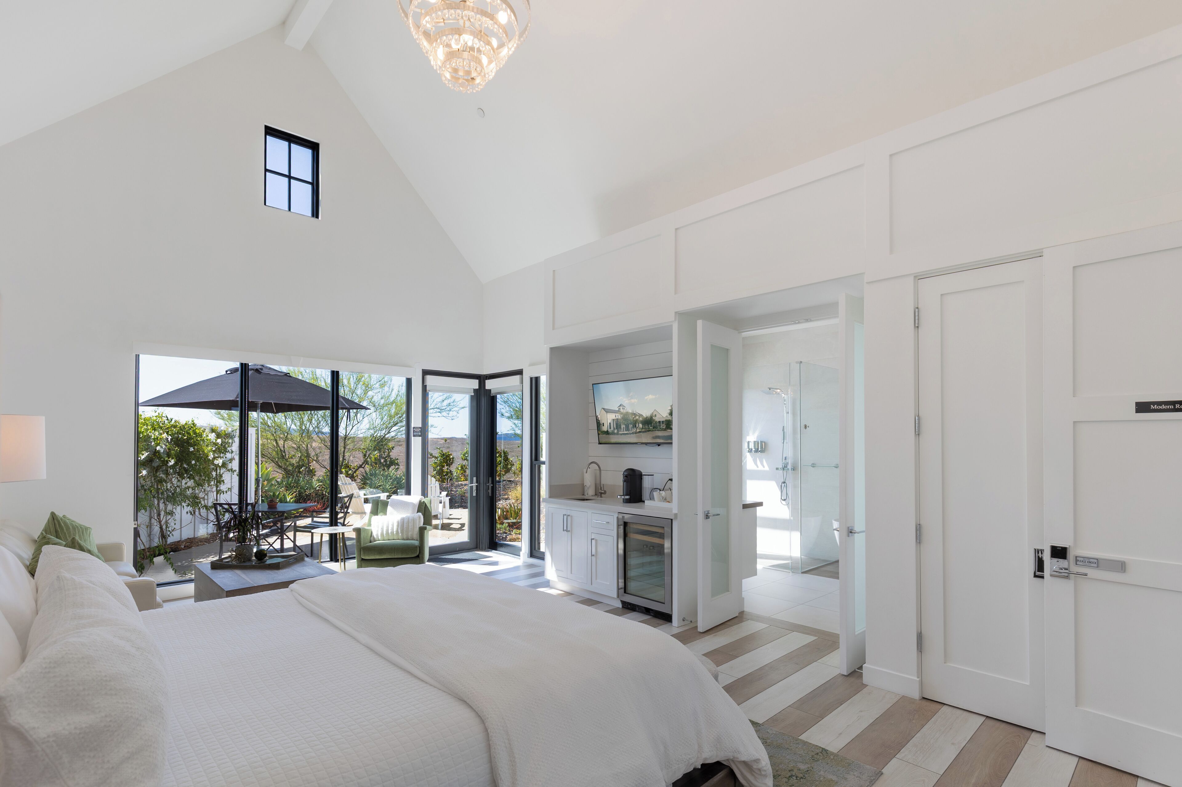 A spacious bedroom with a large bed, a kitchenette, and a sliding glass door leading to a patio area.