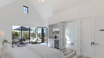 A spacious bedroom with a large bed, a kitchenette, and a sliding glass door leading to a patio area.