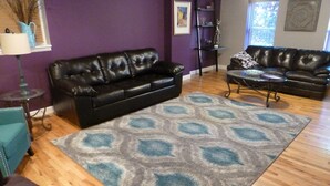 A living room with two black leather sofas, a patterned rug, and wooden flooring. - Fun and walkable area, sleeps 9, private parking and patio, newly renovated! (St. Louis)