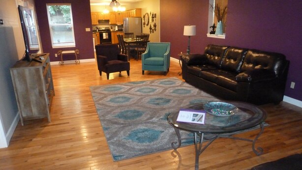 A living room with a black leather couch, a glass coffee table, and a patterned rug. - Fun and walkable area, sleeps 9, private parking and patio, newly renovated! (St. Louis)