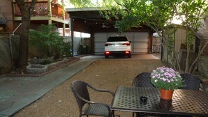 A covered outdoor area with a table and chairs, a potted plant, and a white vehicle parked in the background. - Fun and walkable area, sleeps 9, private parking and patio, newly renovated! (St. Louis)