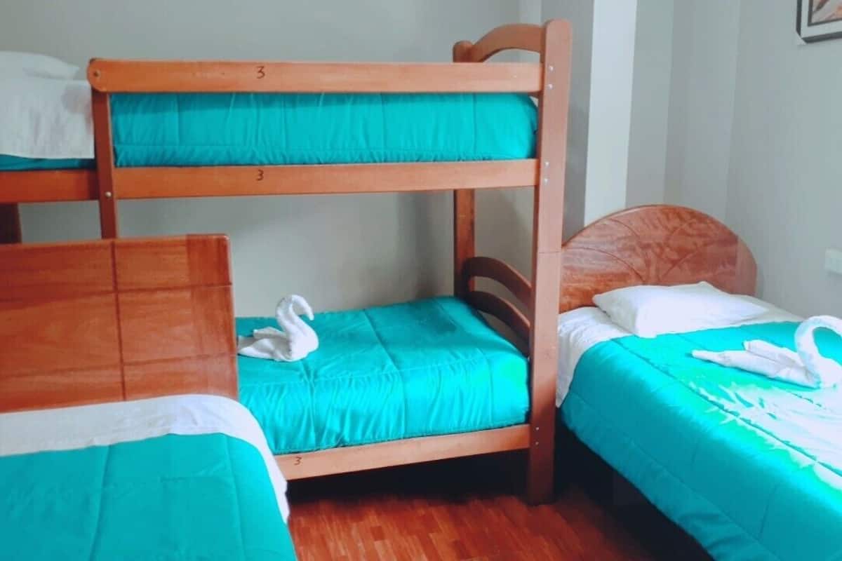 A room with bunk beds and two single beds, each with a teal bedspread and white pillows.