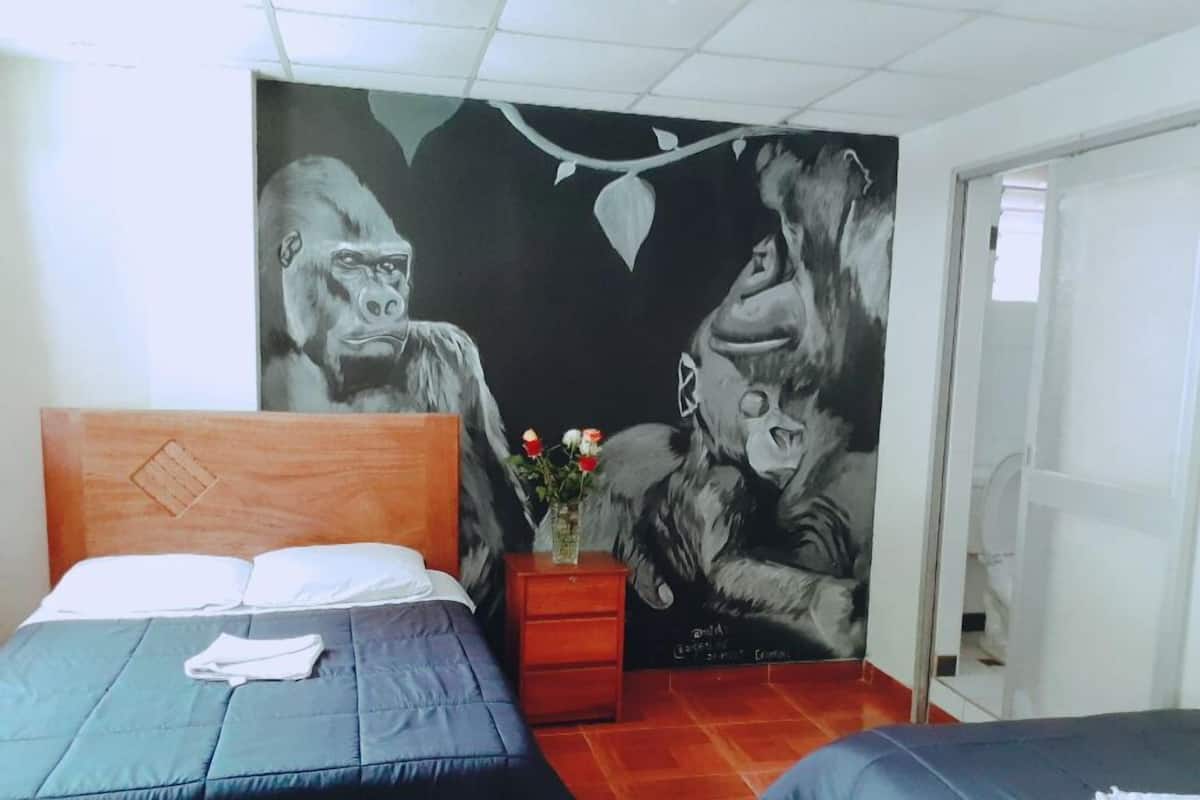 A room with a bed, a nightstand with a vase of flowers, and a mural of gorillas on the wall.