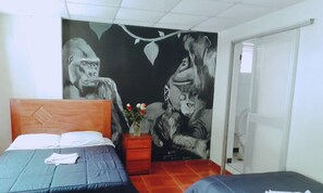 Una habitación con una cama, una mesita de noche con un florero y un mural de gorilas en la pared.