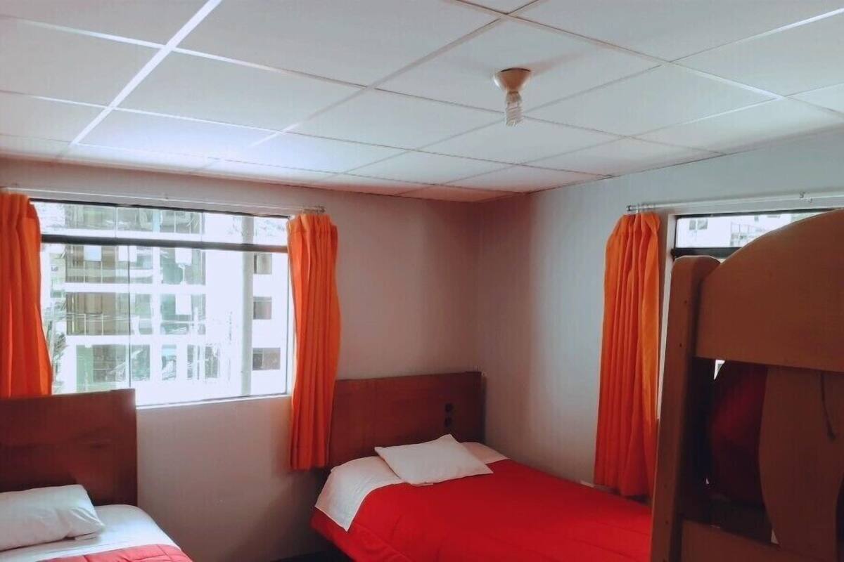 A hotel room with two beds, orange curtains, a wooden headboard, and a window with a view of buildings.