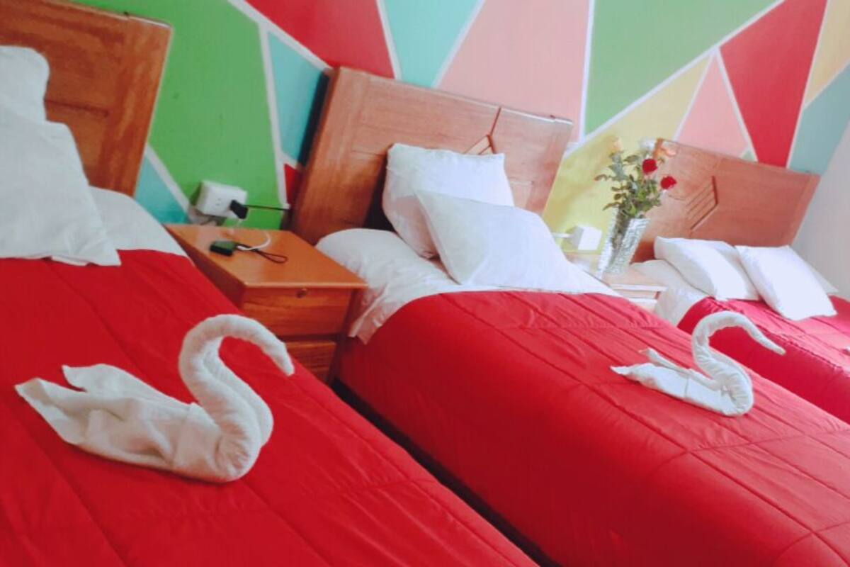 A hotel room with two beds, each with red bedding and white swan-shaped pillows.