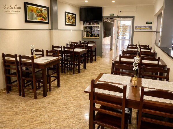 Un'area ristorazione in un hotel con diversi tavoli e sedie in legno, un angolo bar con bottiglie e quadri appesi alle pareti.