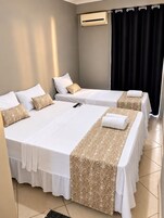 Quarto de hotel com duas camas, ar condicionado fixado na parede e cortina escura.