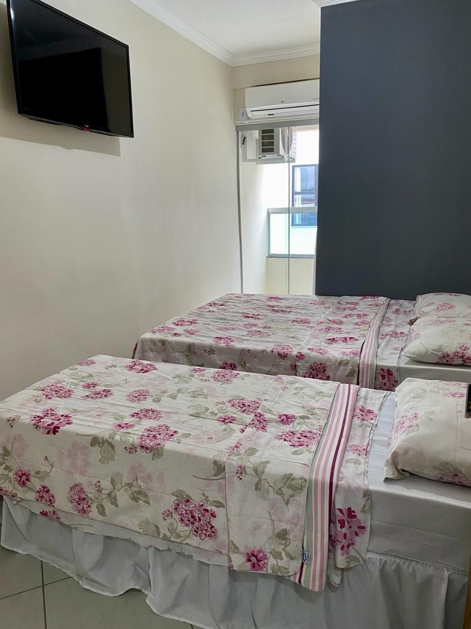 A room with two beds, a flat-screen TV, and an air conditioning unit.