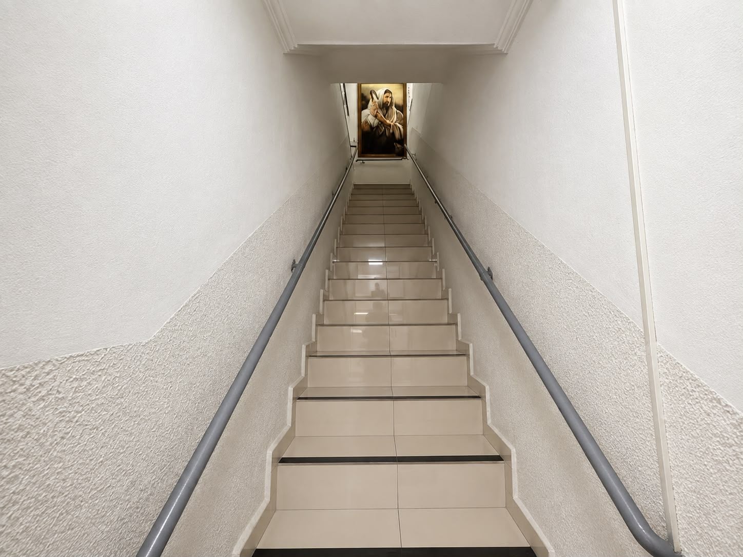 A staircase with beige steps and a handrail, leading to a room with a framed picture on the wall.