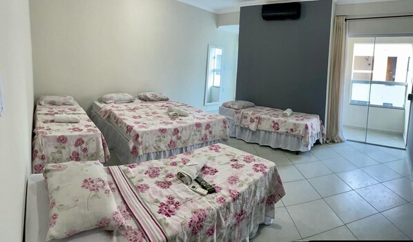 Habitación de hotel con cuatro camas, una mesita pequeña y una puerta corrediza de vidrio que da a un balcón.