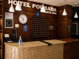 Mostrador de recepción de hotel con un reloj, cartel de tarifas de habitaciones y recordatorio sobre el uso de mascarillas.