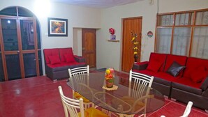 A dining area with a glass table surrounded by white chairs, a red sofa, and a red couch. - CASA GRAU, with 4 rooms with own bathroom, comfortable, central and safe. (Tarapoto)
