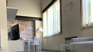 Un vaste espace de vie doté d’un sol carrelé, d’un canapé blanc, d’une table à manger avec des chaises et d’un téléviseur fixé au mur.