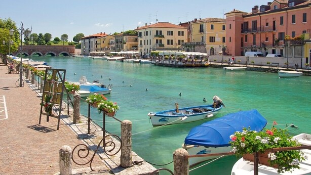 Un canal bordé de bateaux amarrés le long des quais, une promenade piétonne et des bâtiments aux couleurs vives qui bordent l’eau.