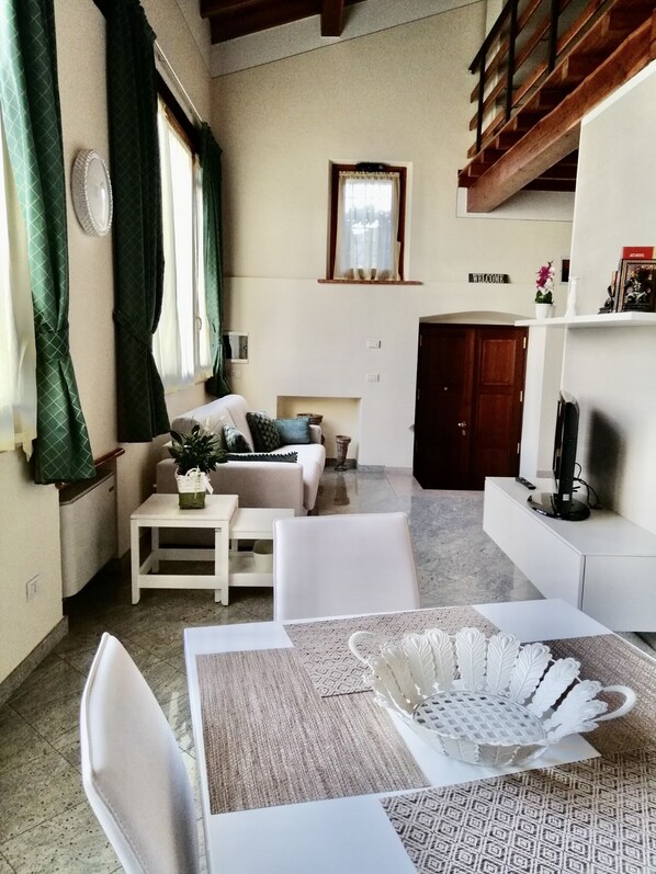 A cozy living room with a sofa, a coffee table, and a dining area with chairs and a patterned table runner.