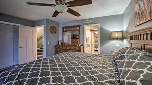 Um quarto com uma cama grande, um ventilador de teto, cômoda, espelho e abajur.