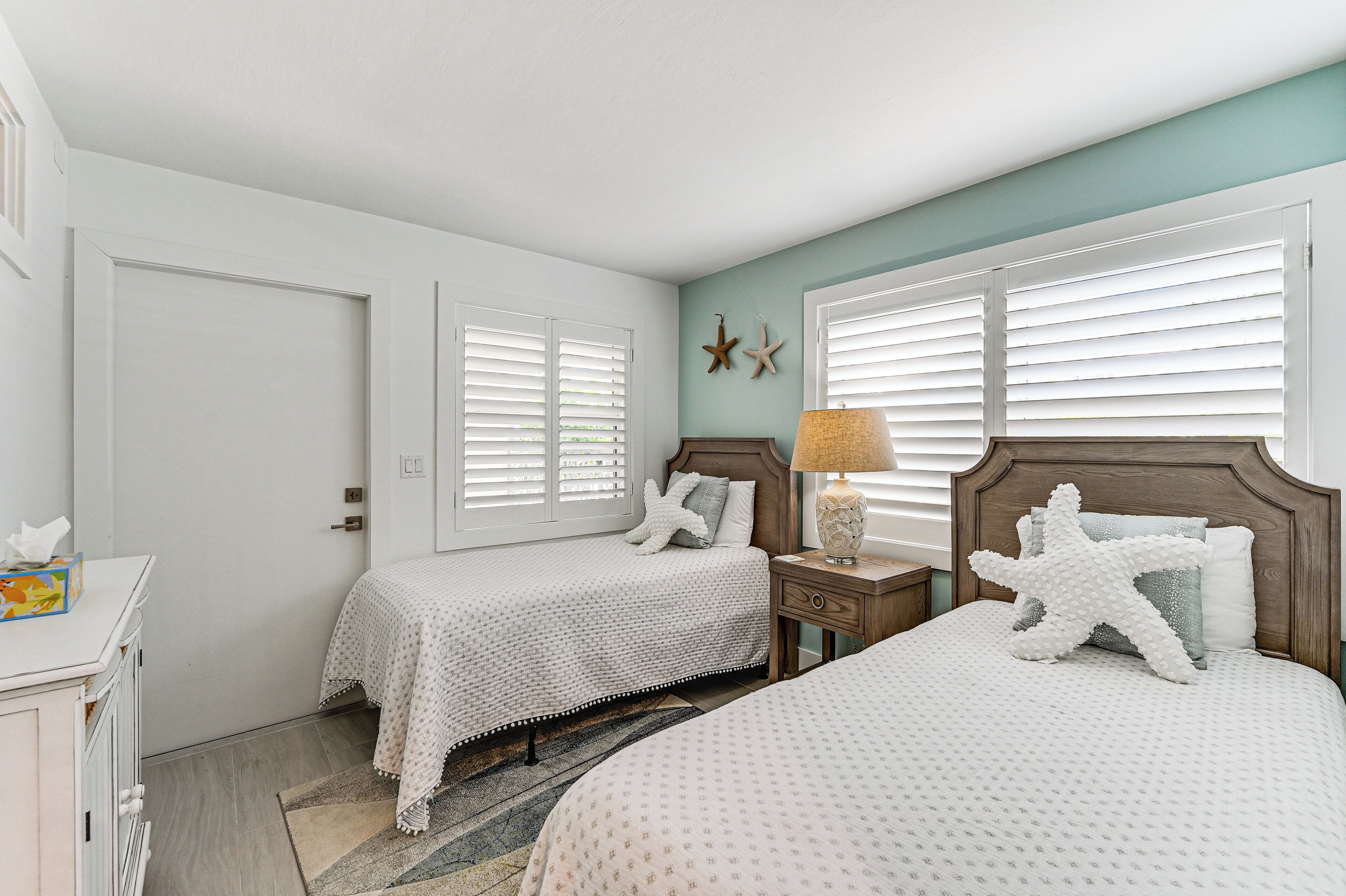 A bedroom with two beds, a nightstand with a lamp, starfish decorations, and a door.