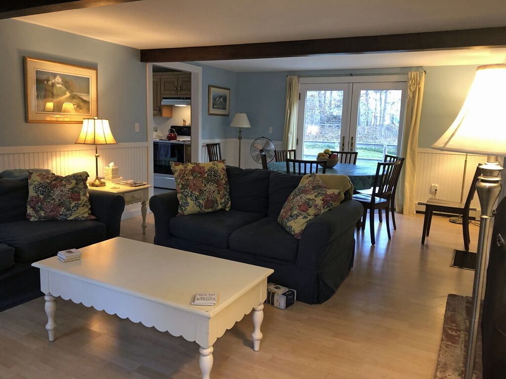 Ein Wohnzimmer mit zwei dunklen Sofas, einem weißen Couchtisch und einem Essbereich mit Tisch und Stühlen.