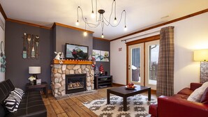 Ein Wohnzimmer mit Kamin aus Stein, einem schwarzen Ledersofa, einem roten Sofa, einem Holztisch und einer Kandelaber.
