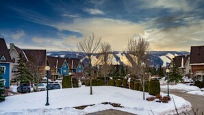 Ein Wohngebiet mit schneebedecktem Boden, Häuser mit traditioneller Architektur und einer Bergkulisse im Hintergrund.